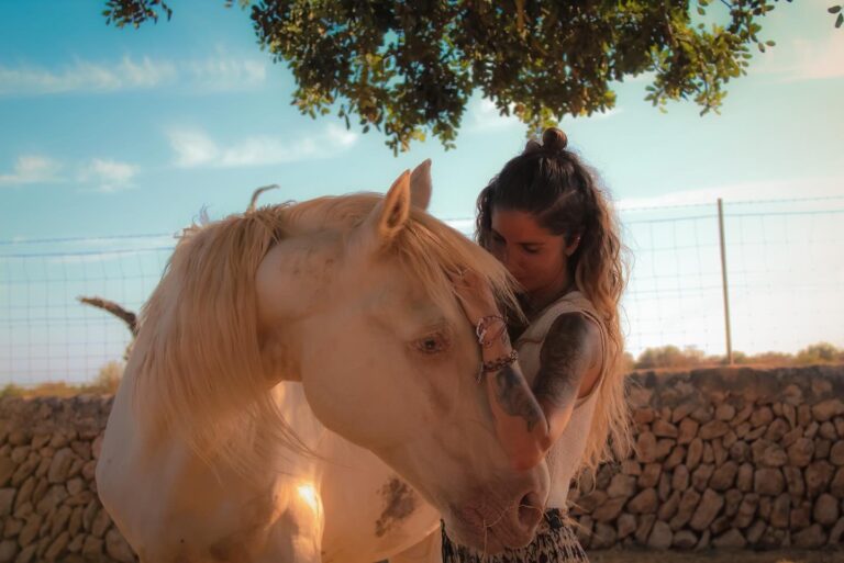 A woman resting her forehead against a palomino horse under a tree