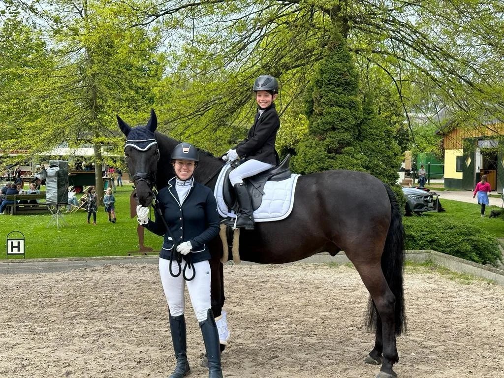 A rider in show dress beside a black Mallorcan horse at a dressage show