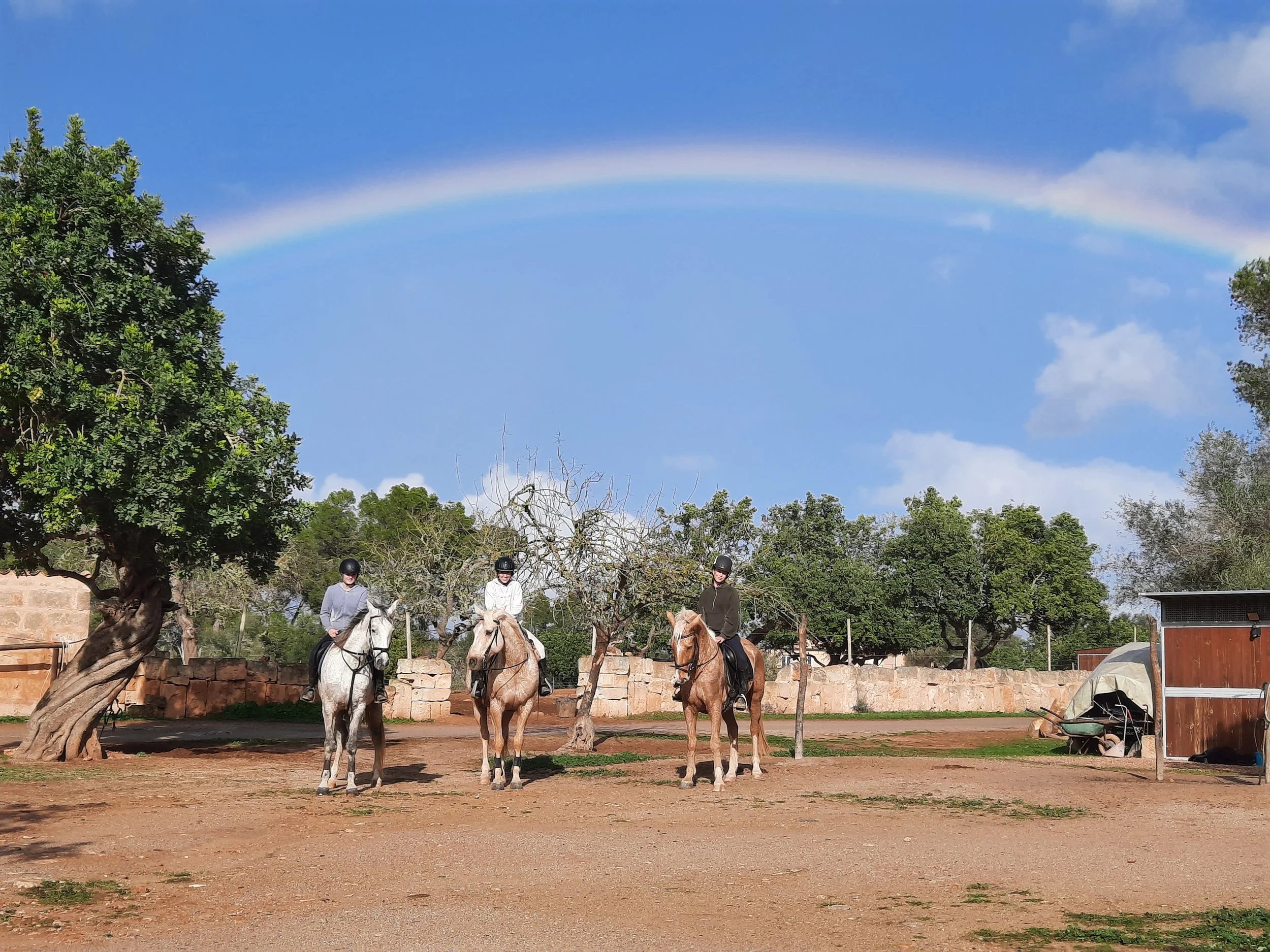 Three riders in the arena at Hackner Ranch under a rainbow