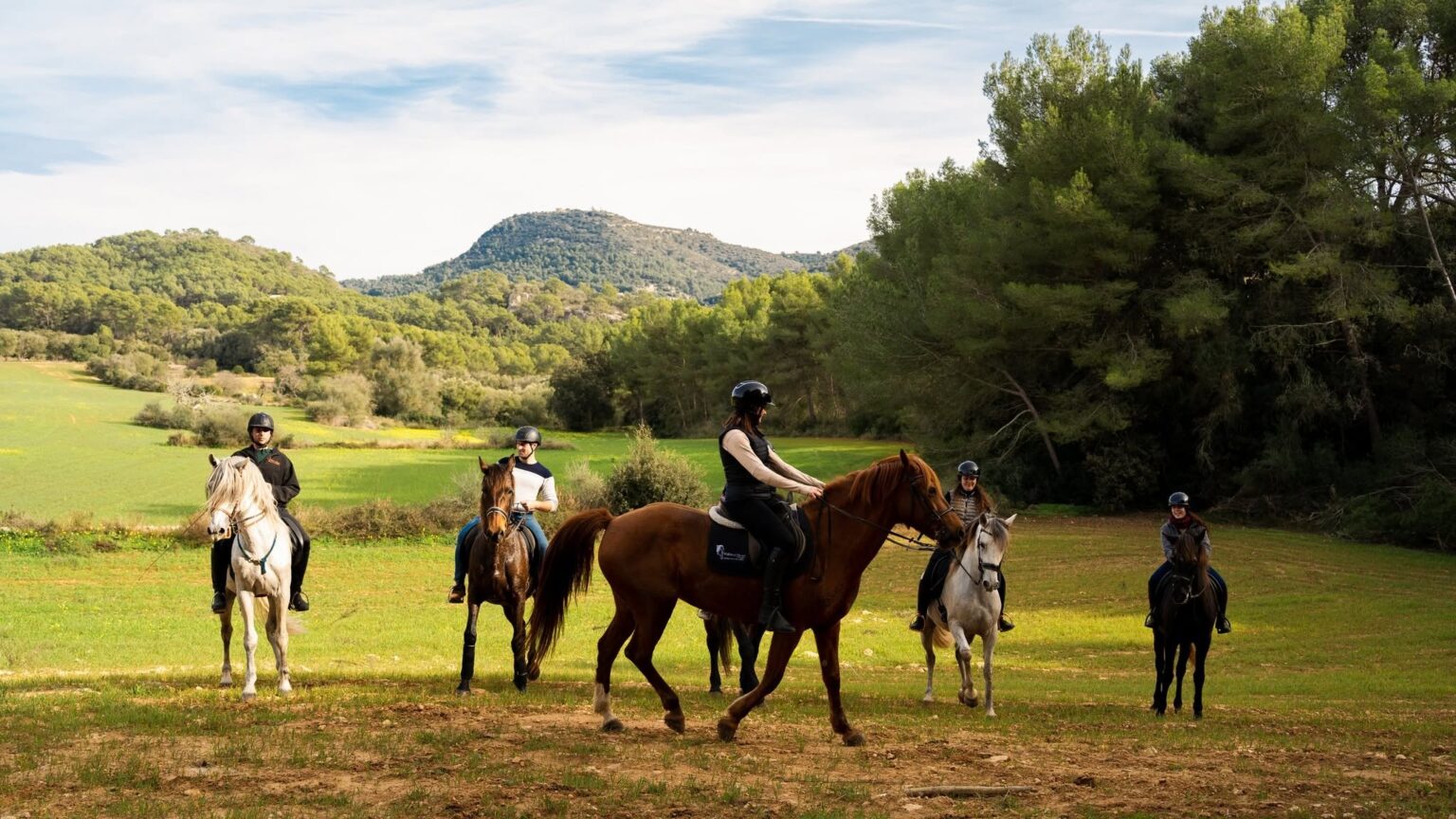 Riders on a green meadow below the hill of Randa