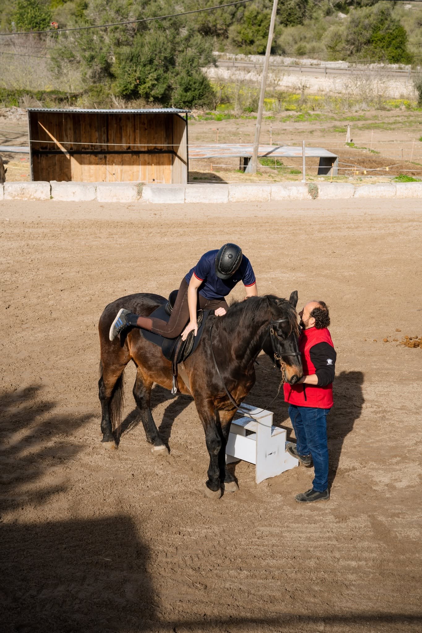 A rider mounts from a block while the instructor holds the horse