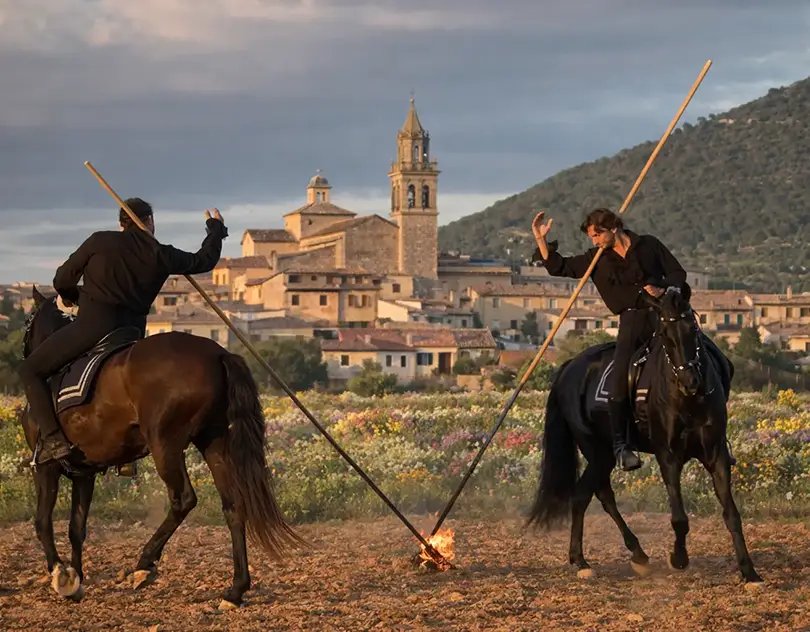 Two riders with lances in a show, a Mallorcan village behind them
