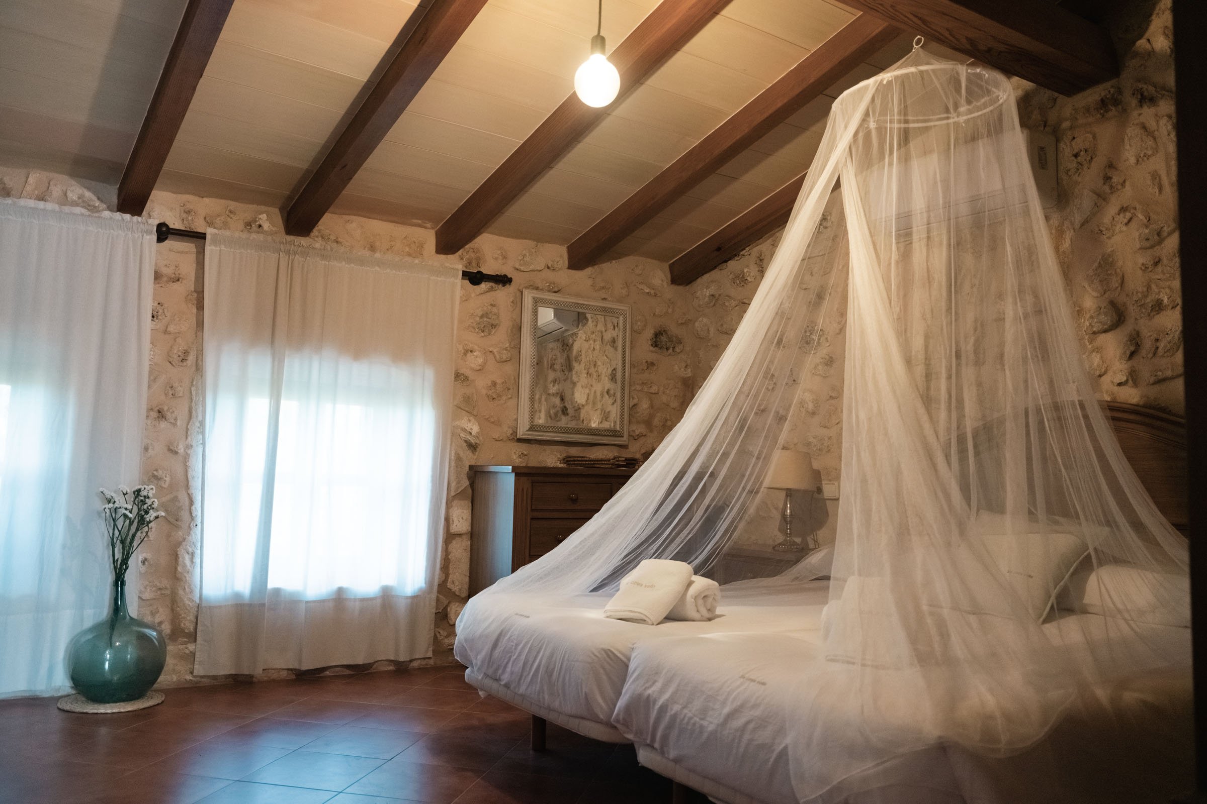 A bedroom under wooden beams with a mosquito net over the bed