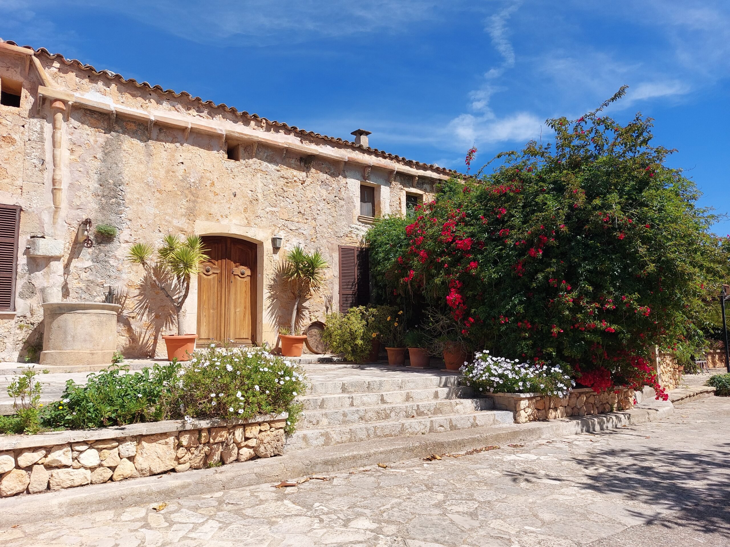 The stone facade and courtyard of Sa Cova Vella with steps, potted plants and bougainvillea