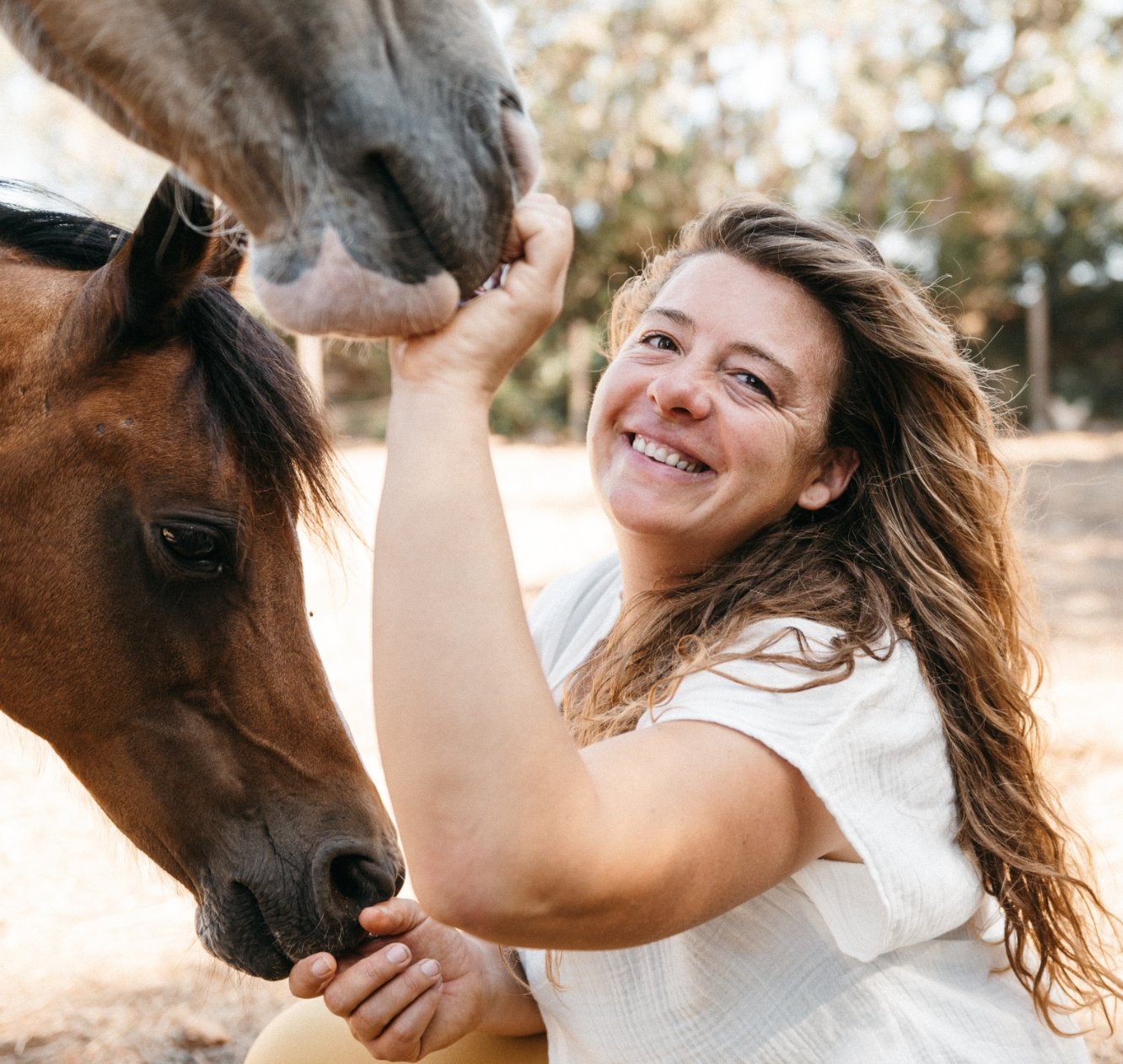 Tamara Scholz laughing while a horse nuzzles her hair
